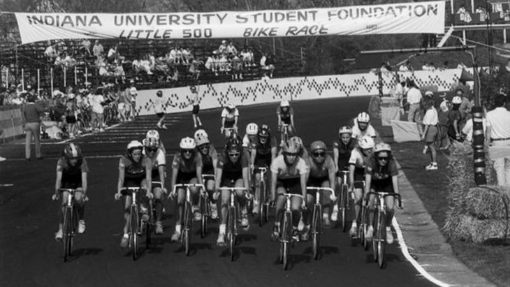A black and white photo of women racing on bikes under a banner that says, “Indiana University Student Foundation Little 500 Bike Race”